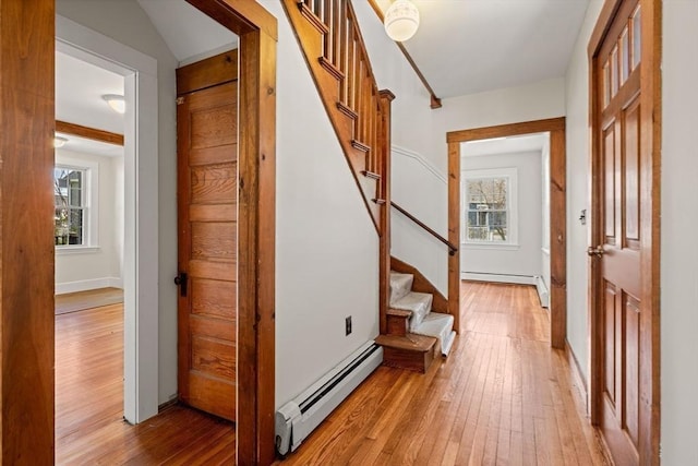 hall featuring stairs, a baseboard heating unit, baseboard heating, light wood finished floors, and baseboards