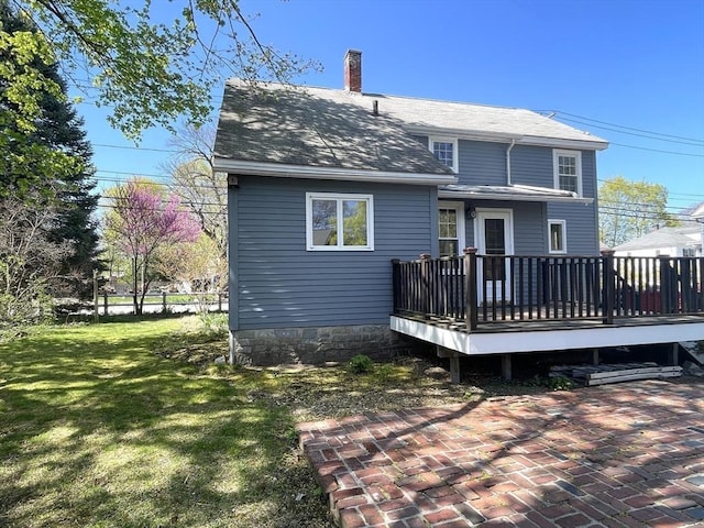 rear view of property featuring a chimney, a yard, a shingled roof, a wooden deck, and a patio area