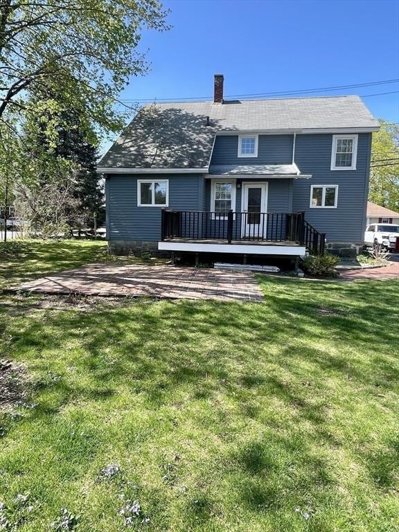 back of property with a lawn, a deck, a shingled roof, and a chimney