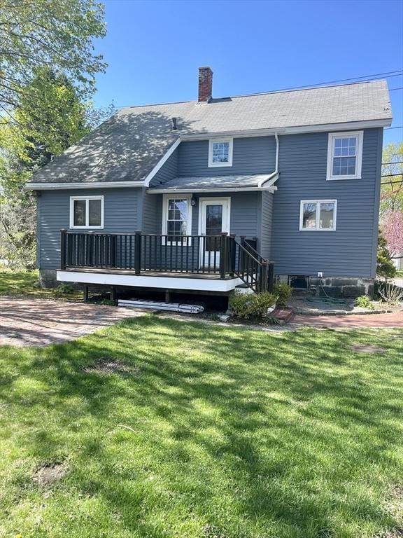 rear view of property featuring a lawn, a wooden deck, and a chimney