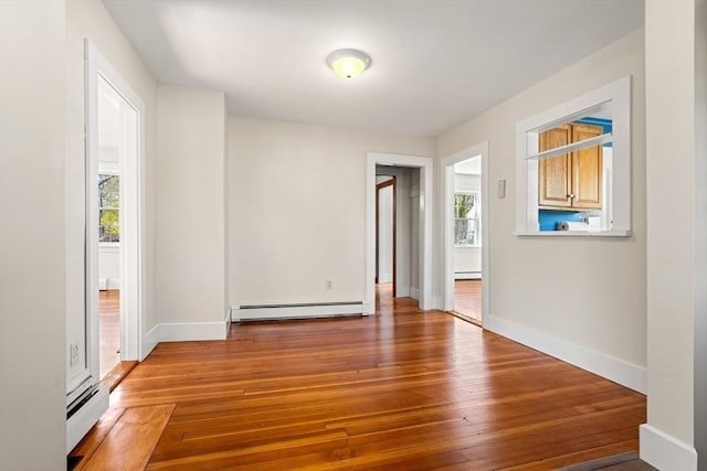 empty room with a wealth of natural light, baseboards, a baseboard heating unit, and wood-type flooring