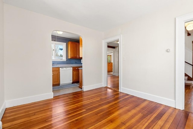 unfurnished living room with baseboards, arched walkways, and light wood-style flooring