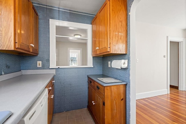 kitchen featuring arched walkways, light countertops, brown cabinets, white dishwasher, and dark wood-type flooring