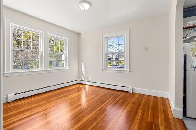 spare room with a baseboard radiator, a healthy amount of sunlight, and hardwood / wood-style flooring