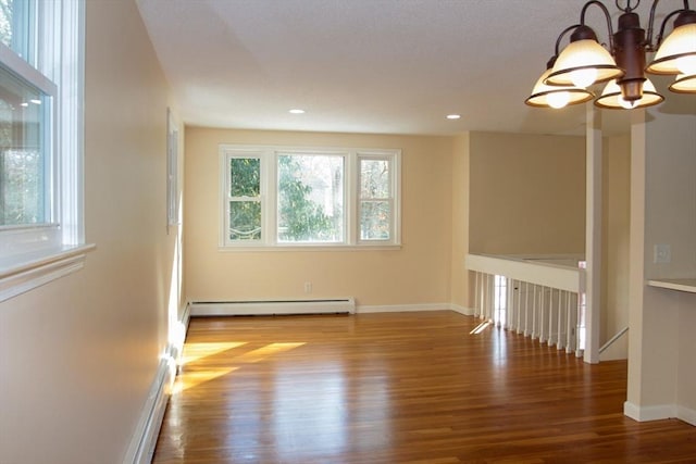 empty room with a baseboard radiator, hardwood / wood-style flooring, and an inviting chandelier