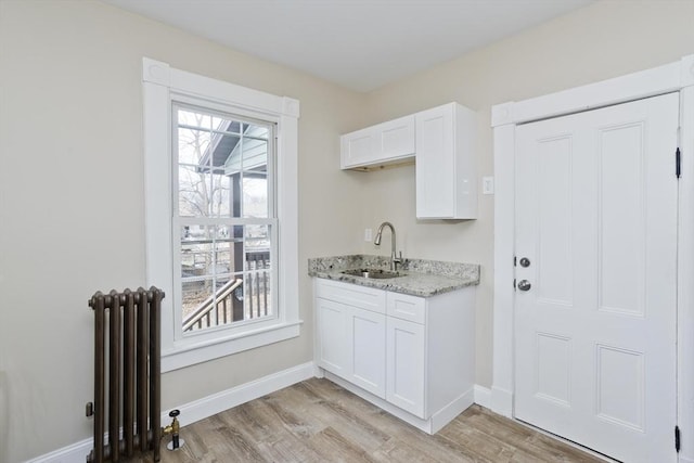 kitchen with white cabinetry, sink, light stone counters, and radiator heating unit