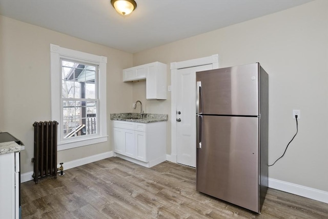 kitchen with light stone countertops, stainless steel refrigerator, radiator heating unit, and white cabinetry