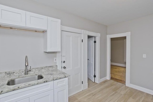 kitchen featuring white cabinets, light stone countertops, and sink