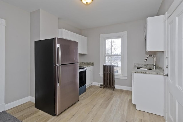 kitchen with white cabinetry, light hardwood / wood-style floors, appliances with stainless steel finishes, sink, and radiator heating unit