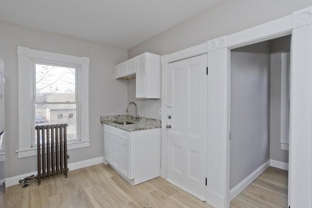 kitchen featuring radiator, white cabinets, light stone counters, and sink