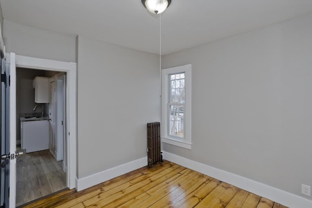 empty room featuring hardwood / wood-style flooring, sink, and radiator heating unit