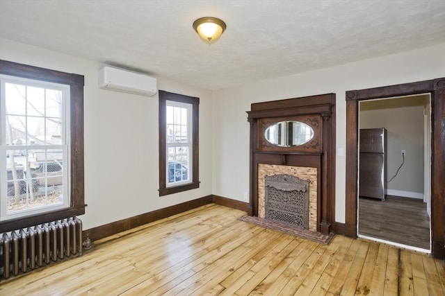 unfurnished living room with plenty of natural light, light wood-type flooring, radiator heating unit, and a wall mounted air conditioner