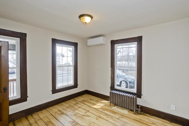 empty room with an AC wall unit, plenty of natural light, radiator heating unit, and light hardwood / wood-style floors