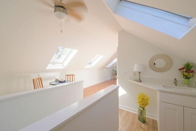 interior space with sink, vaulted ceiling with skylight, light wood-type flooring, and ceiling fan