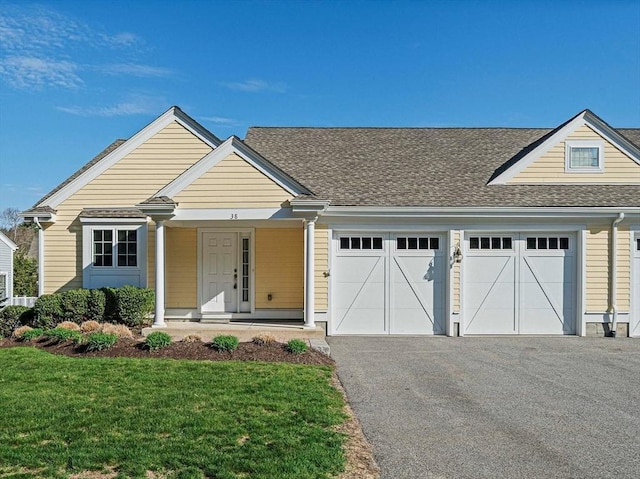 view of front of property featuring a garage, a front lawn, a shingled roof, a porch, and driveway
