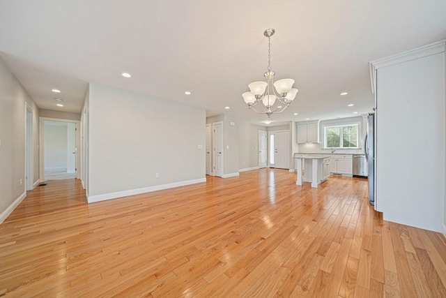 unfurnished living room featuring an inviting chandelier, recessed lighting, light wood-style floors, and baseboards