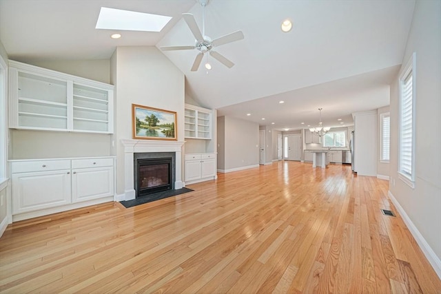 unfurnished living room featuring visible vents, recessed lighting, light wood-type flooring, vaulted ceiling with skylight, and a fireplace with flush hearth
