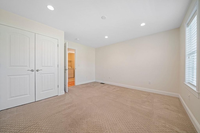 unfurnished bedroom featuring a closet, baseboards, multiple windows, and light carpet