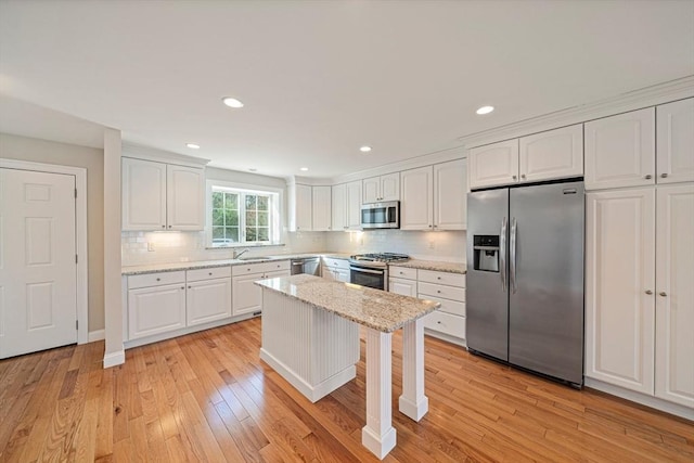 kitchen with decorative backsplash, appliances with stainless steel finishes, a sink, white cabinets, and light wood-style flooring