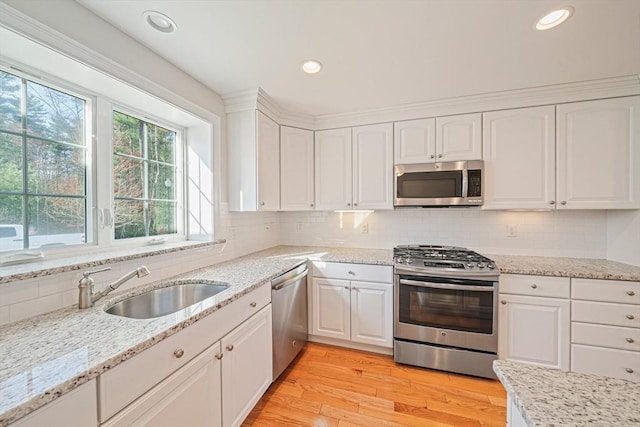 kitchen featuring tasteful backsplash, a sink, light wood finished floors, stainless steel appliances, and white cabinetry
