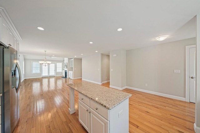 kitchen with open floor plan, stainless steel refrigerator with ice dispenser, white cabinetry, light wood finished floors, and a notable chandelier