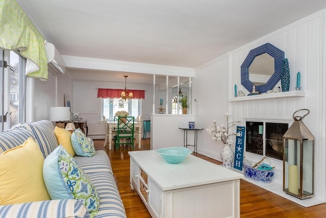 living room with a chandelier, a wall mounted air conditioner, wood finished floors, and a fireplace with flush hearth