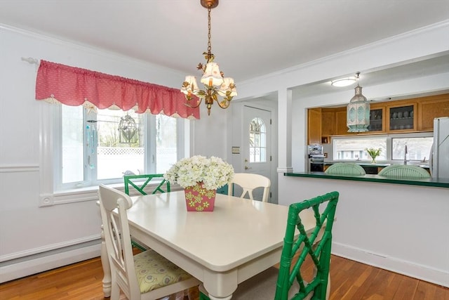 dining area featuring wood finished floors, a chandelier, crown molding, and a baseboard heating unit