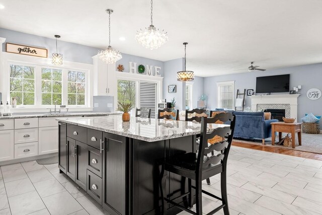 15 Day Lily Ln, Walpole, MA 02081 - kitchen featuring light marble finish floors, a chandelier, a ceiling fan, a tile fireplace, and white cabinetry