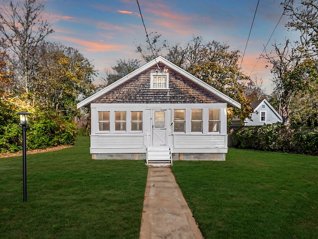 back house at dusk featuring a lawn