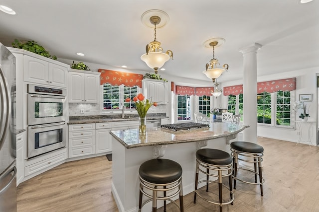 kitchen featuring light hardwood / wood-style floors, backsplash, hanging light fixtures, white cabinetry, and appliances with stainless steel finishes