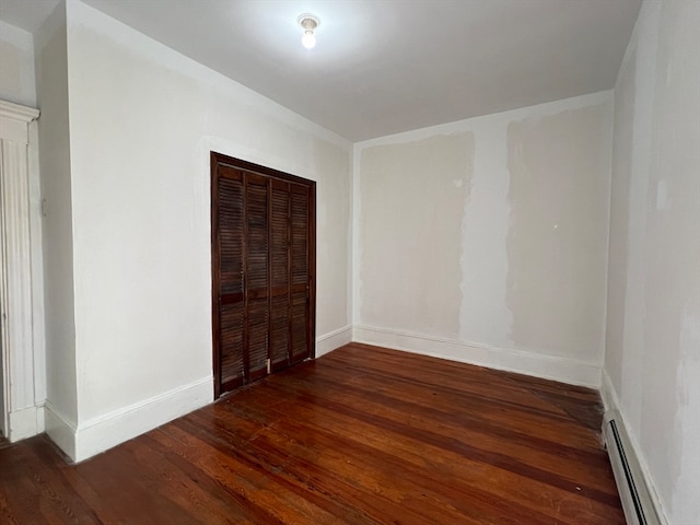 unfurnished bedroom featuring a baseboard radiator, a closet, and dark hardwood / wood-style floors