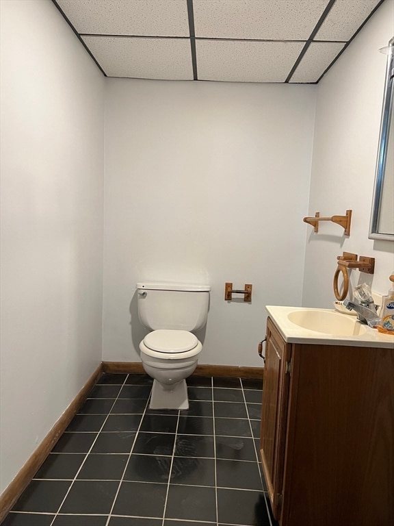 bathroom with a drop ceiling, tile patterned floors, toilet, and vanity