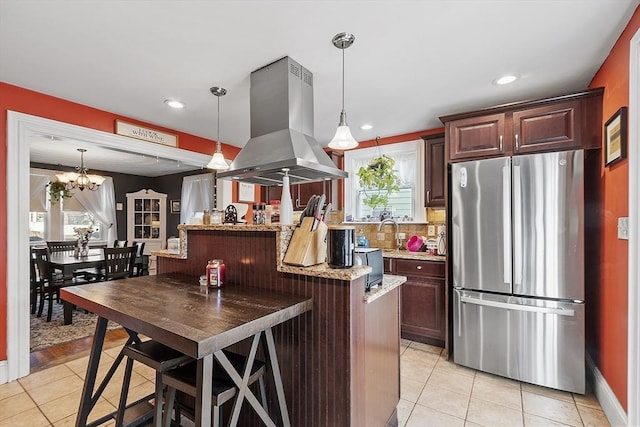 kitchen with island exhaust hood, decorative light fixtures, an inviting chandelier, stainless steel refrigerator, and light tile patterned flooring