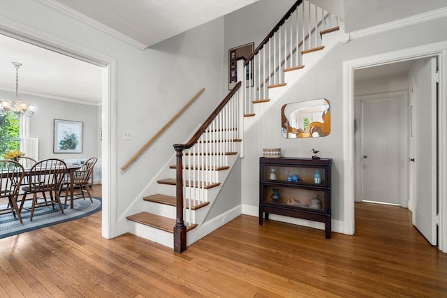 stairway featuring wood-type flooring, ornamental molding, baseboards, and a chandelier