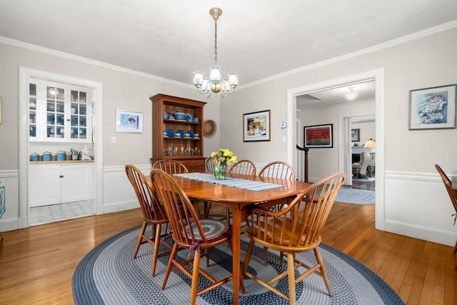 dining room with light wood finished floors, ornamental molding, a chandelier, and wainscoting