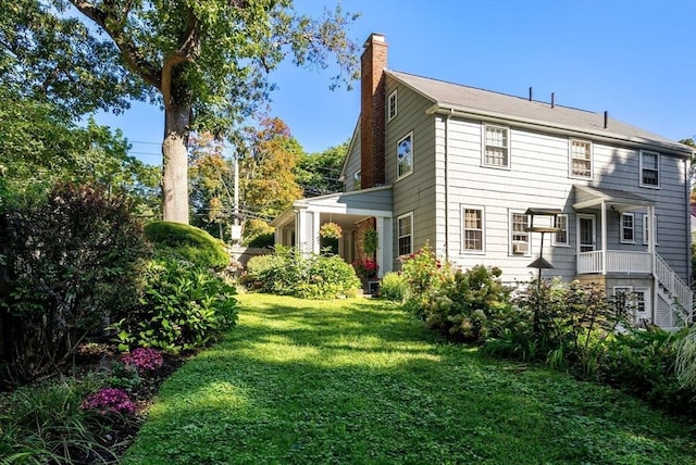 back of house featuring a chimney and a lawn