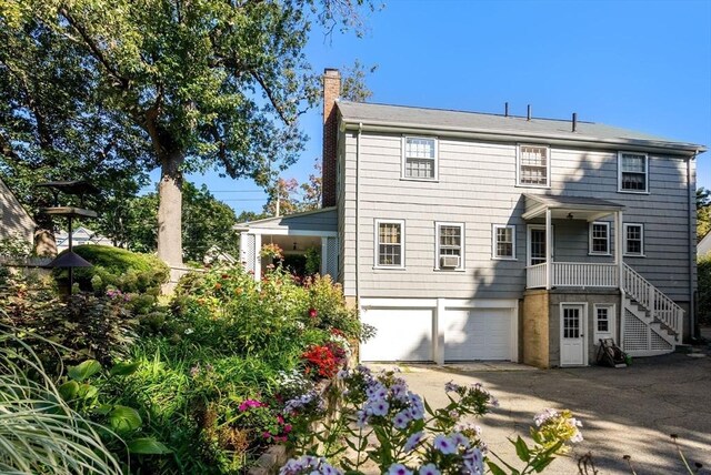 back of house featuring a chimney, an attached garage, driveway, and stairway