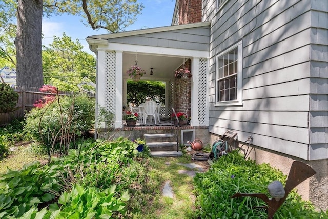 view of exterior entry featuring covered porch, fence, and a chimney