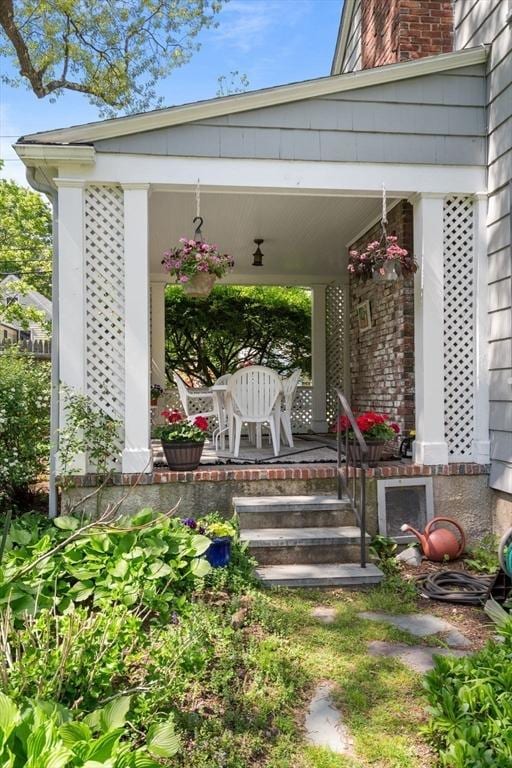 entrance to property with a porch, a chimney, and brick siding
