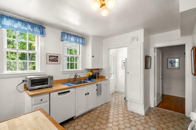 kitchen with white dishwasher, a sink, white cabinetry, wood counters, and light tile patterned floors