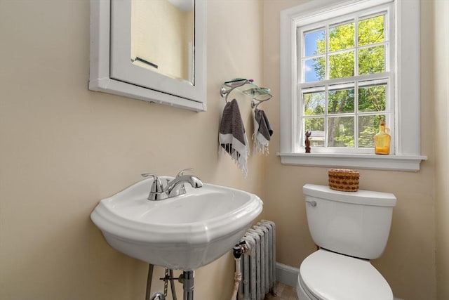 half bath with radiator, toilet, a sink, and baseboards
