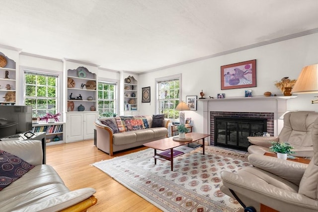 living area with crown molding, light wood-style floors, a brick fireplace, and healthy amount of natural light