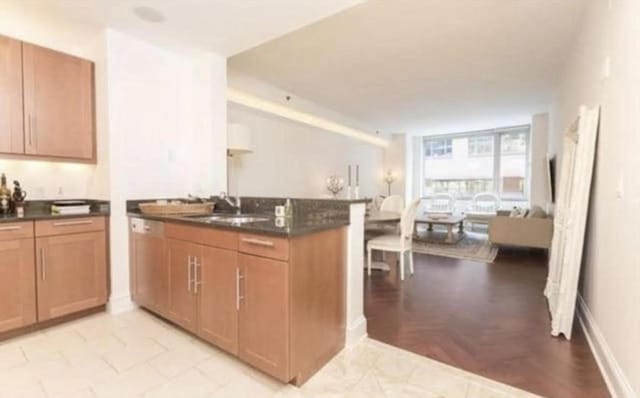 kitchen featuring baseboards, a peninsula, a sink, dark countertops, and open floor plan