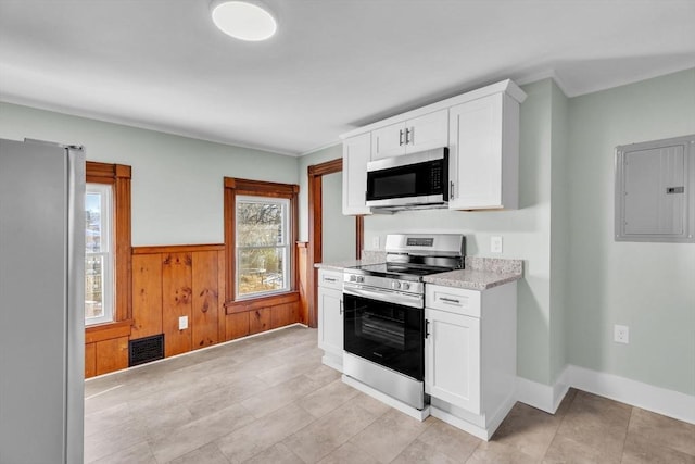 kitchen featuring electric panel, wooden walls, white cabinetry, a healthy amount of sunlight, and appliances with stainless steel finishes