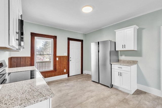 kitchen featuring light stone counters, appliances with stainless steel finishes, white cabinets, and wooden walls