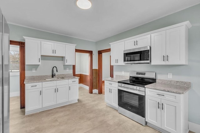 kitchen with light stone countertops, stainless steel appliances, white cabinetry, and sink