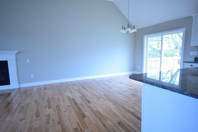 unfurnished living room with an inviting chandelier, vaulted ceiling, and light hardwood / wood-style flooring