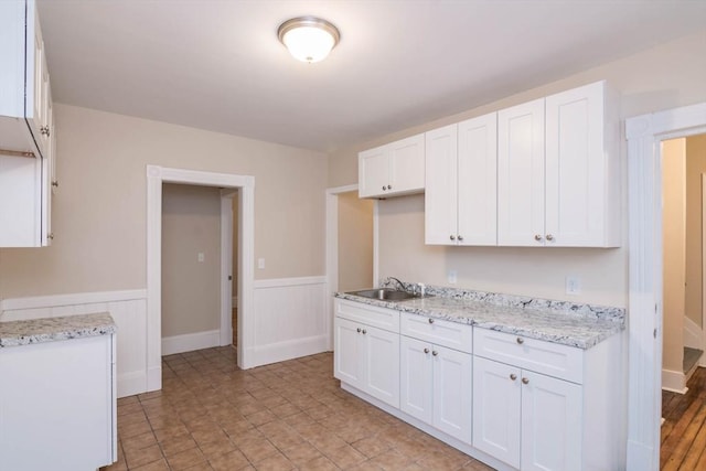 kitchen featuring light stone countertops, white cabinetry, and sink