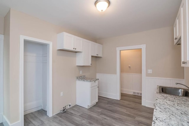 kitchen featuring light stone countertops, light hardwood / wood-style floors, white cabinetry, and sink