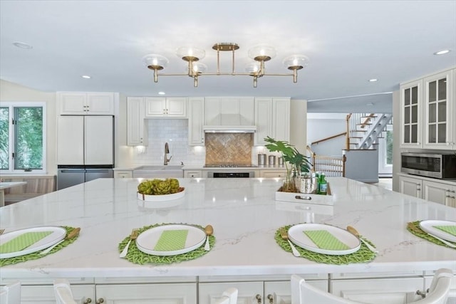 kitchen with glass insert cabinets, light stone counters, stainless steel microwave, white fridge, and a sink